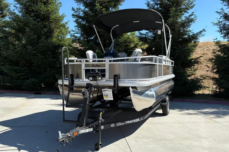 Slide: The Image of 2026 Sun Tracker Bass Buggy 18 DLX pontoon boat on trailer, parked outdoors. - 4