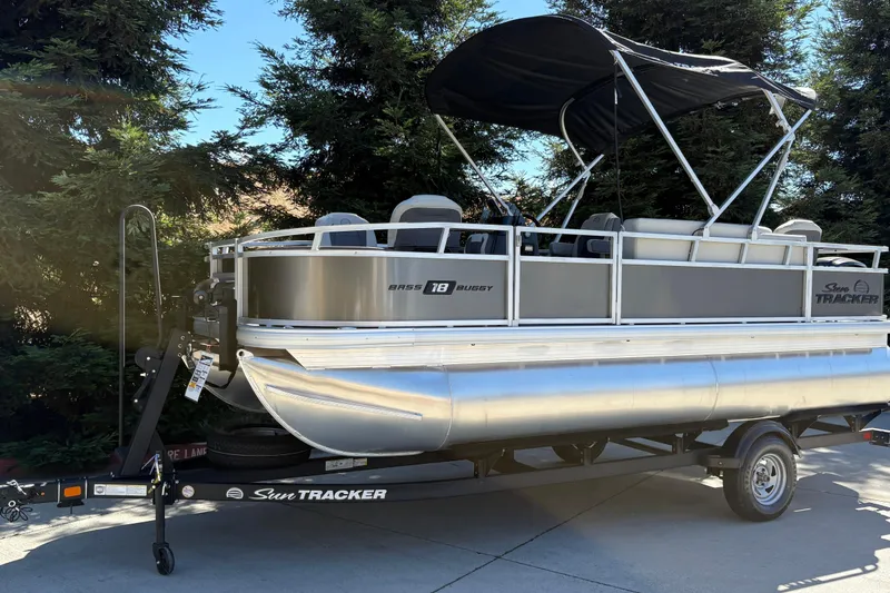 Slide: The Image of 2026 Sun Tracker Bass Buggy 18 DLX pontoon boat on trailer, parked outdoors. - 10
