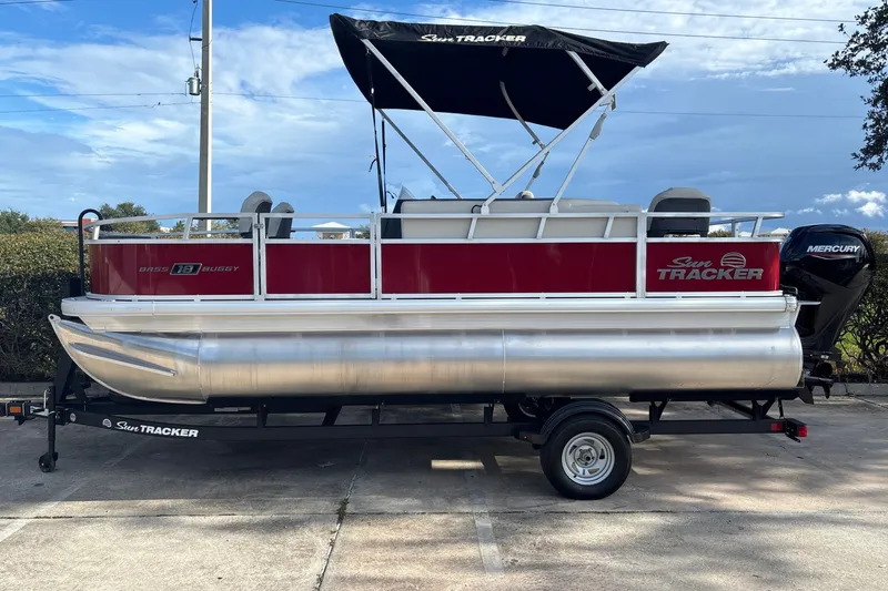 The Image of 2026 Sun Tracker Bass Buggy 18 DLX pontoon boat on trailer, featuring Mercury outboard motor. - 0