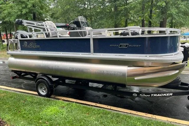 Slide: The Image of 2026 Sun Tracker Bass Buggy 18 DLX pontoon boat on trailer, parked outdoors. - 1