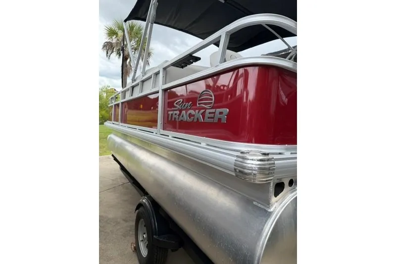 Slide: The Image of 2026 Sun Tracker Bass Buggy 18 DLX pontoon boat, red exterior, parked outdoors. - 3