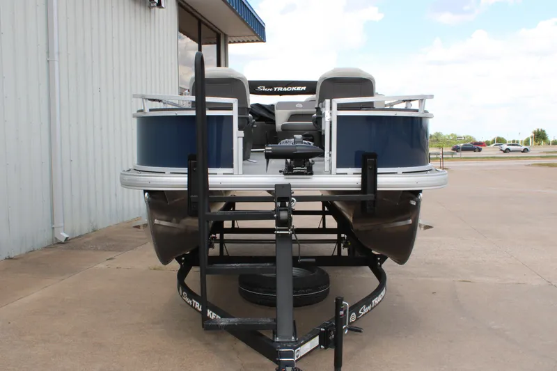 Slide: The Image of 2026 Sun Tracker Bass Buggy 18 DLX pontoon boat on trailer, parked outdoors. - 2