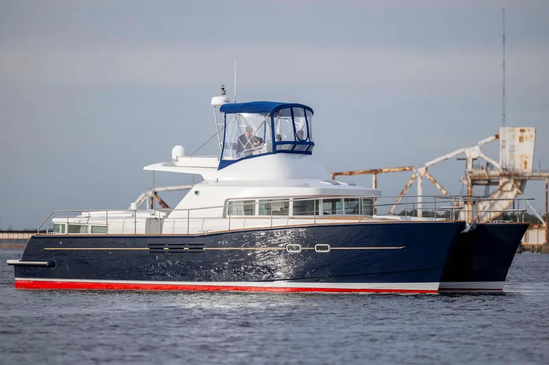 Slide: The Image of 2004 Lagoon 43 PC yacht with blue hull and red trim on calm water. - 11