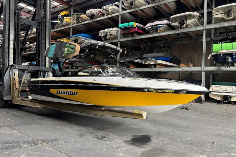 Slide: The Image of 2005 Malibu Wakesetter VLX boat in storage, lifted by forklift, surrounded by other boats. - 4