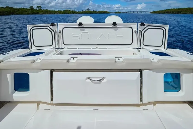 Slide: The Image of 2022 Solace 41 CS boat deck with storage compartments open, on a serene water backdrop. - 17