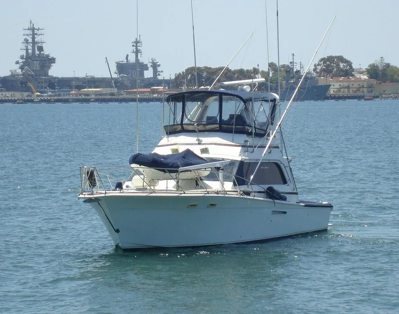 Slide: The Image of 1987 Egg Harbor Sportfisher boat on calm water with naval ships in the background. - 1
