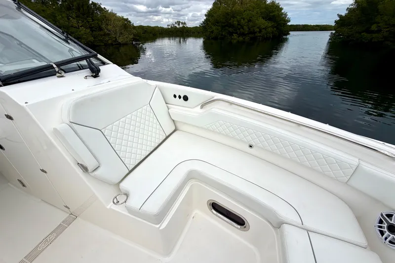 Slide: The Image of 2024 Pursuit DC 365 Dual Console boat interior with white seating, near lush waterway. - 21