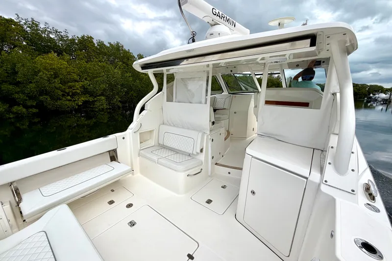 Slide: The Image of 2024 Pursuit DC 365 Dual Console boat interior with seating and storage, near lush greenery. - 9