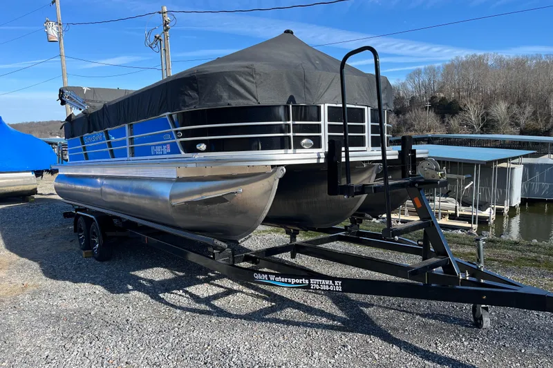 Slide: The Image of 2023 Berkshire 24RFX LE pontoon boat on trailer, covered, near a lake. - 1