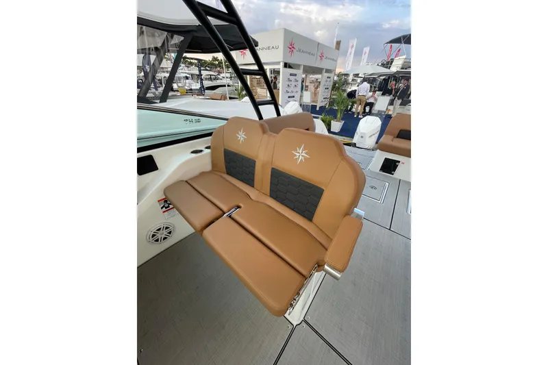 Slide: The Image of 2026 Jeanneau TH33 boat interior with tan seating and logo, displayed at a boat show. - 23