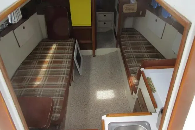 Slide: The Image of 1974 Pearson 30 sailboat interior with twin plaid beds and compact kitchenette. - 11