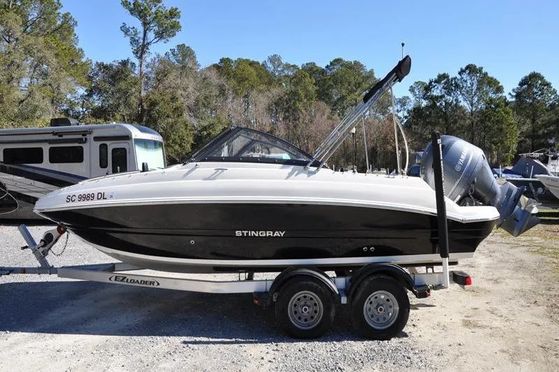 Slide: The Image of 2021 Stingray 201 DS boat on trailer, parked outdoors with trees in background. - 6