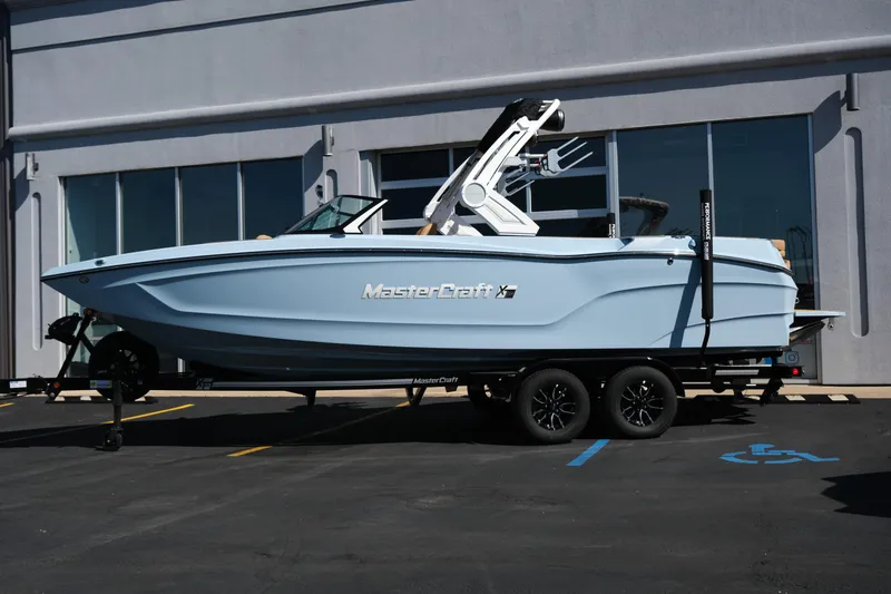 Slide: The Image of 2026 MasterCraft XT24 boat on trailer, parked outside a building. - 1