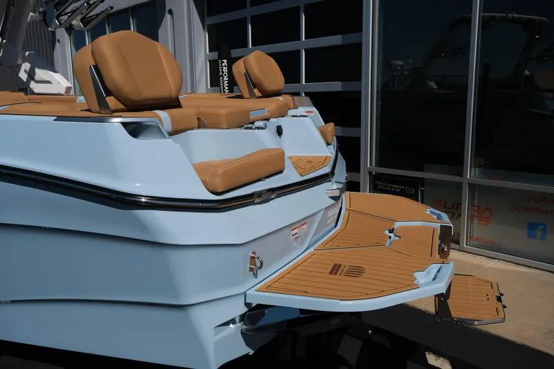 Slide: The Image of 2026 MasterCraft XT24 boat with tan seats and swim platform, docked near a glass building. - 8