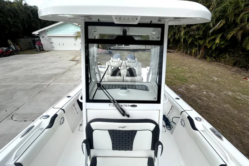 Slide: The Image of 2022 Tidewater 256 CC Adventure boat, white interior, parked near a garage and greenery. - 11