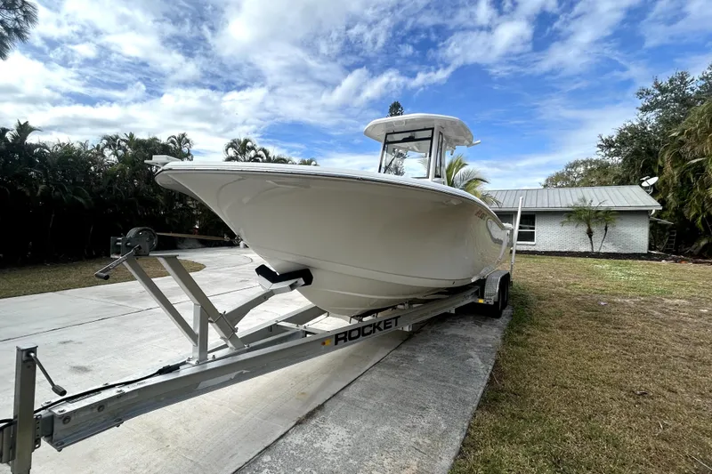 Slide: The Image of 2022 Tidewater 256 CC Adventure boat on trailer, parked in driveway under cloudy sky. - 18