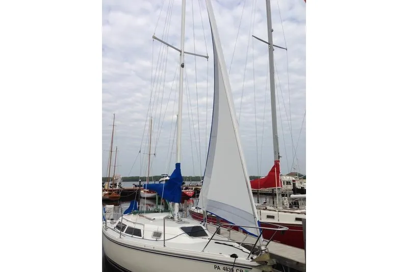 Slide: The Image of 1993 Catalina 28 sailboat docked with sails raised, under a cloudy sky. - 32