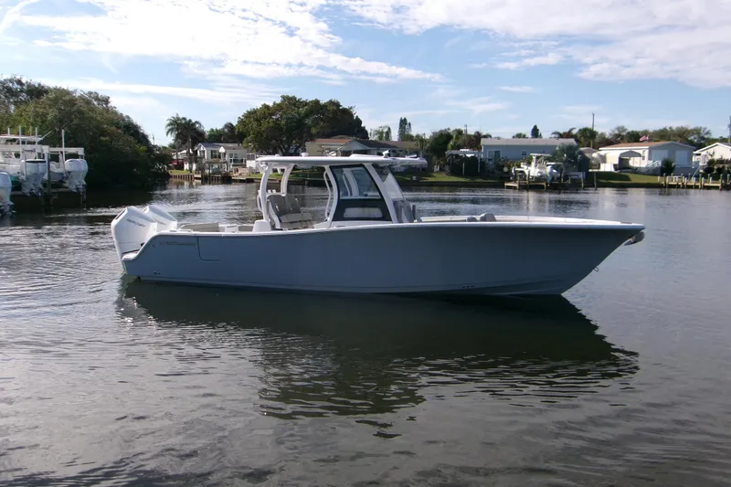 Slide: The Image of 2025 Sportsman Open 322 Center Console boat on calm water, surrounded by trees and houses. - 2