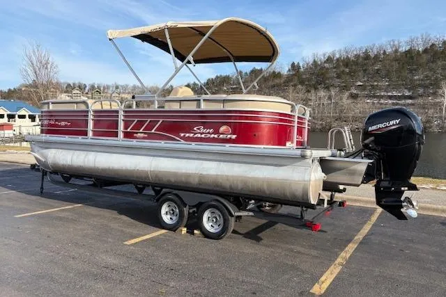 Slide: The Image of 2023 Sun Tracker Party Barge 22 DLX pontoon boat on trailer, parked near a lake. - 2