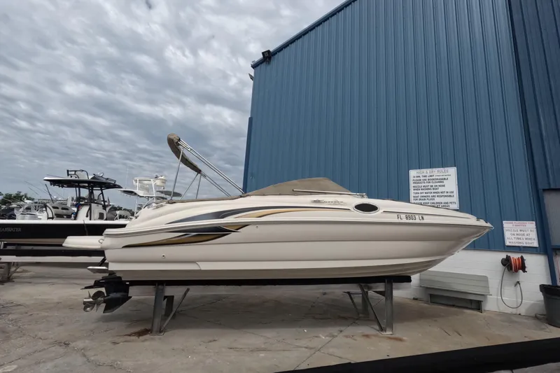 The Image of 2001 Sea Ray 240 Sundeck boat on dry dock near blue building under cloudy sky. - 0