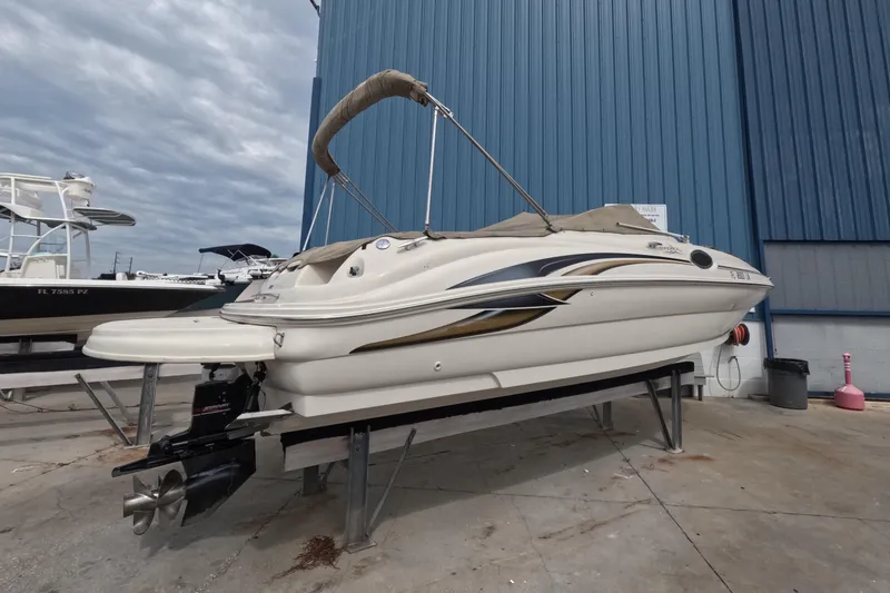 Slide: The Image of 2001 Sea Ray 240 Sundeck boat on a lift, docked near a blue building. - 2