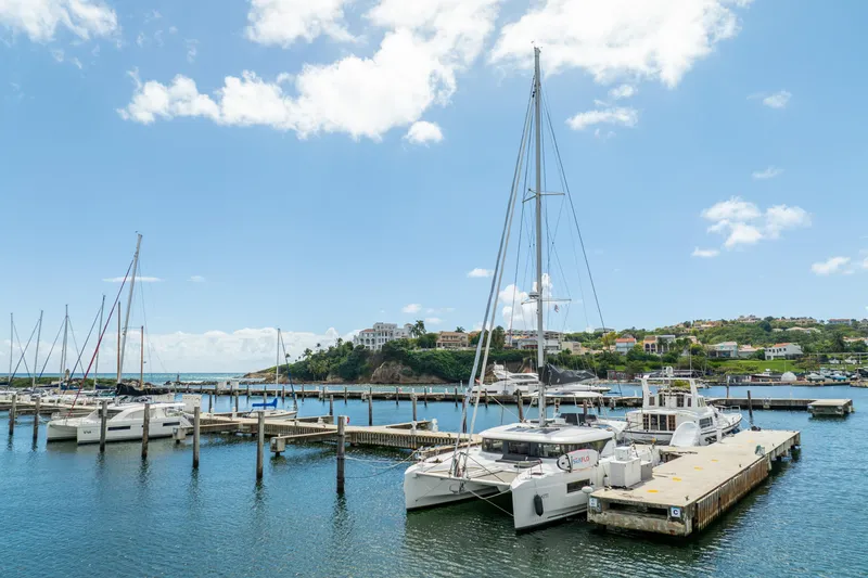 Slide: The Image of 2023 Lagoon 46 catamaran docked in a scenic marina under a clear blue sky. - 118