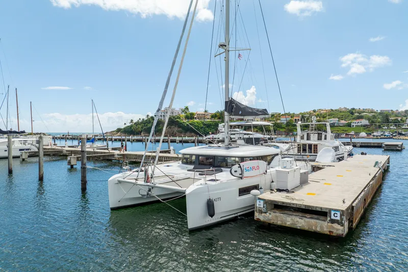 Slide: The Image of 2023 Lagoon 46 catamaran docked at a marina under a clear blue sky. - 119