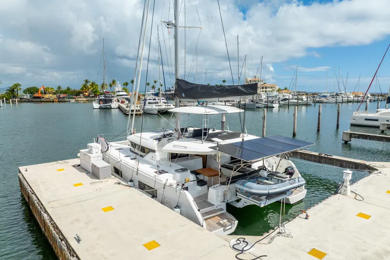 Slide: The Image of 2023 Lagoon 46 catamaran docked in a marina, featuring solar panels and a dinghy. - 121