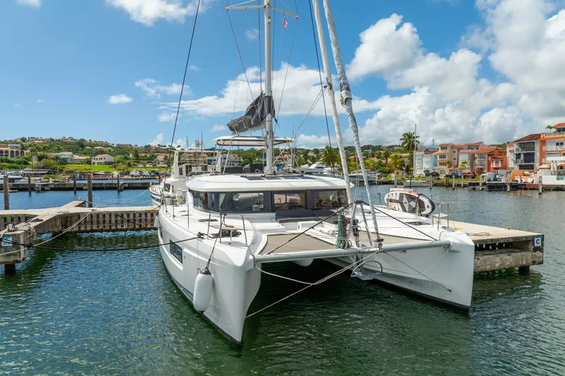 Slide: The Image of 2023 Lagoon 46 catamaran docked in a scenic marina under a bright blue sky. - 124