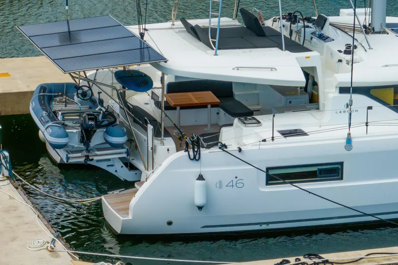 Slide: The Image of 2023 Lagoon 46 catamaran docked, featuring solar panels and an attached dinghy. - 128