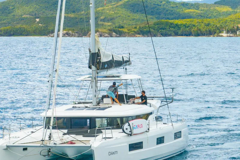 Slide: The Image of 2023 Lagoon 46 catamaran sailing near lush green island coast. - 130