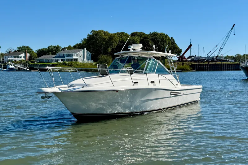 The Image of 2000 Pursuit 3000 Express boat on calm water near shoreline homes and cranes. - 0