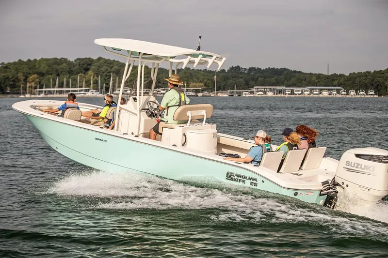 Slide: The Image of 2026 Carolina Skiff 26 Ultra Elite boat with Suzuki outboard motor displayed indoors. - 2