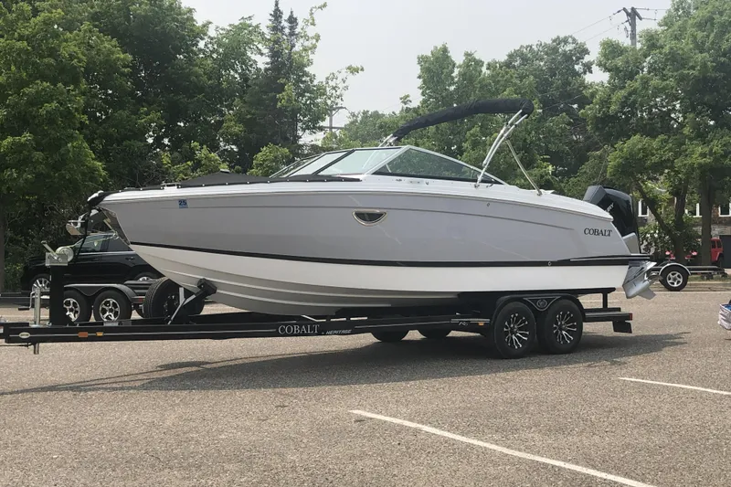 The Image of 2023 Cobalt R6 Outboard boat on trailer in parking lot, surrounded by trees. - 0