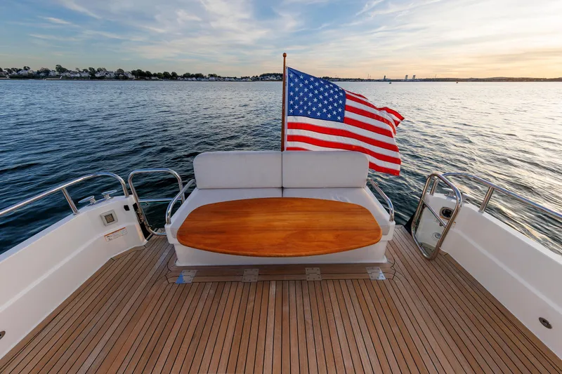 Slide: The Image of 2022 Sabre 38 SE yacht deck with American flag, wooden table, and scenic water view. - 7