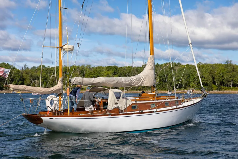 Slide: The Image of 1957 Sparkman & Stephens K/CB Yawl sailing on a scenic lake with lush green shoreline. - 24