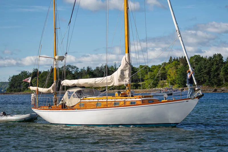 Slide: The Image of 1957 Sparkman & Stephens K/CB Yawl sailboat on serene water with lush green backdrop. - 27