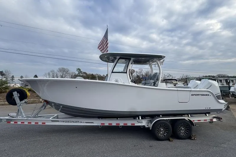 The Image of 2026 Sportsman Open 282 Center Console boat on trailer, American flag, cloudy sky. - 0
