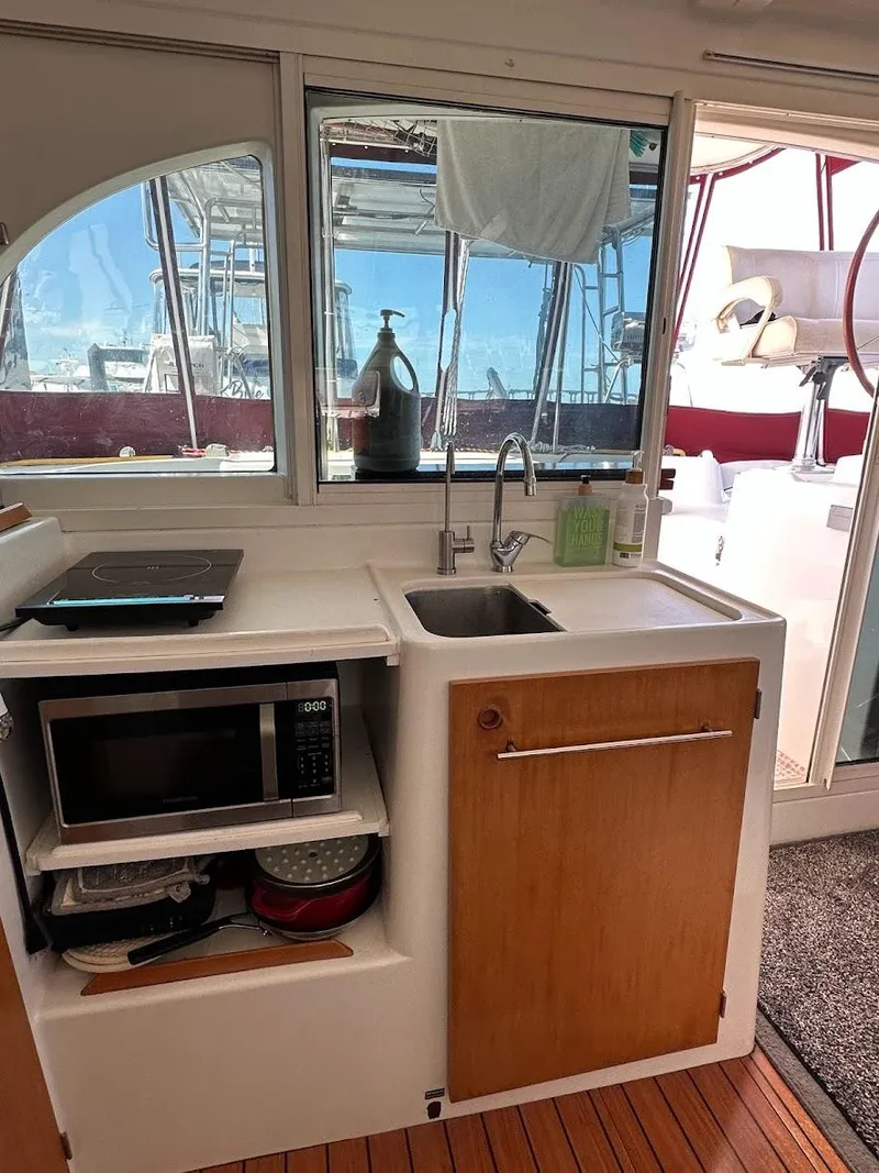 Slide: The Image of Lagoon 380 (2004) yacht kitchen with sink, microwave, and outdoor view. - 15