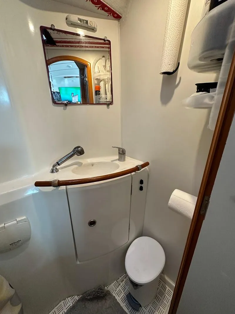 Slide: The Image of Compact bathroom in a 2004 Lagoon 380 catamaran, featuring a sink, mirror, and toilet. - 26