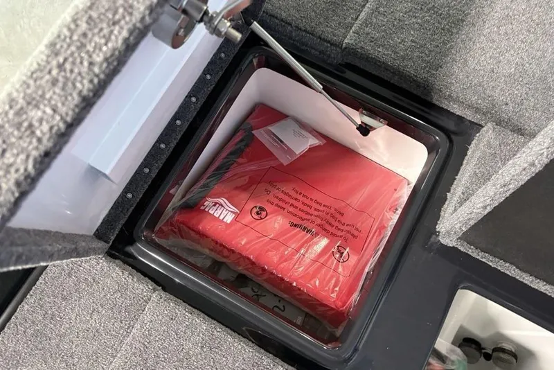 Slide: The Image of Open storage compartment in a 2026 Phoenix 919 ZXL boat, containing a red marine safety kit. - 29