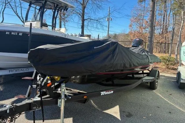 Slide: The Image of 2022 Triton 18 TrX boat covered on trailer, parked outdoors near trees. - 3