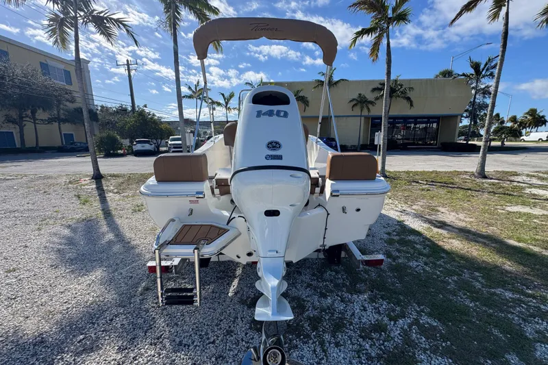 Slide: The Image of 2026 Pioneer 180 Islander boat with 140 HP engine, parked outdoors under palm trees. - 3