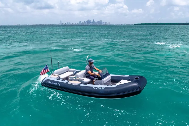 Slide: The Image of Man piloting a Williams tender boat on turquoise waters, city skyline in background. - 57