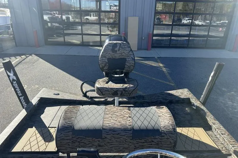 Slide: The Image of 2026 Xpress H190B Bay boat with camo seats, parked outside a garage. - 12