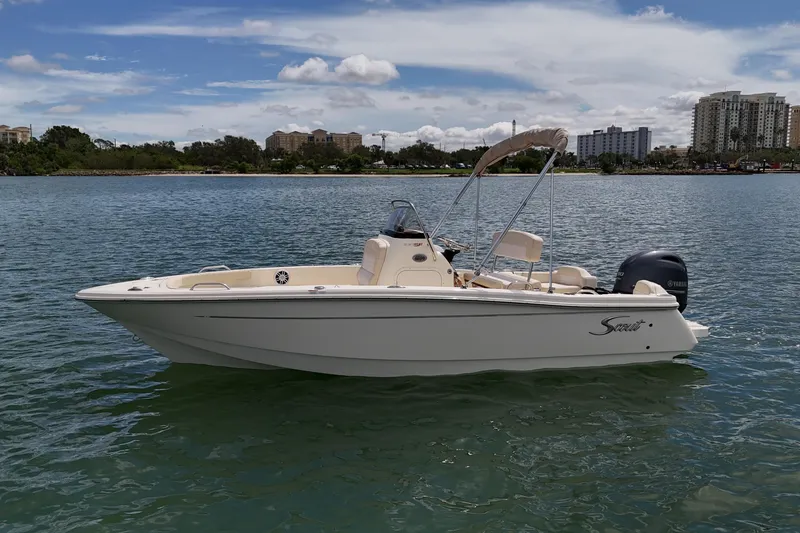 Slide: The Image of 2026 Scout 188 Sportfish boat on calm water with cityscape background. - 2
