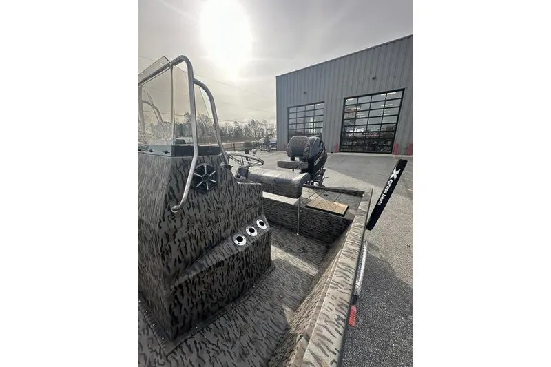 Slide: The Image of 2026 Xpress H190B Bay boat with camouflage design, parked outside a warehouse. - 3
