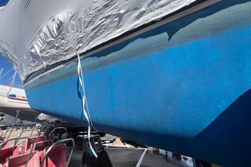 Slide: The Image of 1996 Caliber 35 LRC sailboat hull in dry dock, partially covered, with blue paint. - 51