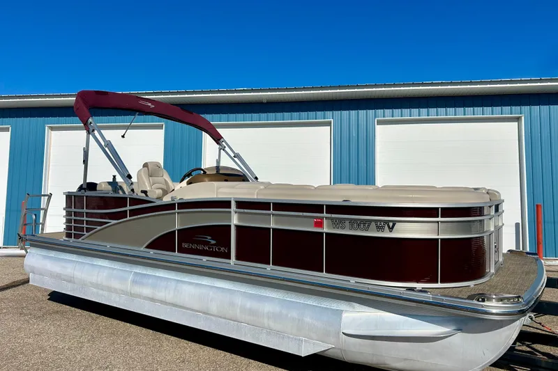 The Image of 2016 Bennington R21 pontoon boat with maroon canopy, parked near blue garage doors. - 1
