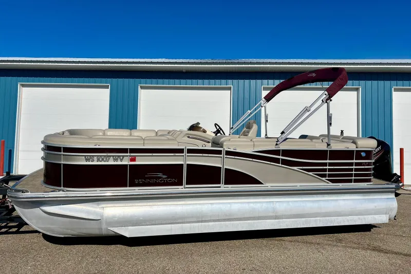 Slide: The Image of 2016 Bennington R21 pontoon boat with maroon canopy, parked near blue building. - 23